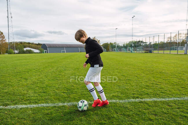 Vista laterale del giocatore di calcio adolescente attivo che calcia la palla durante l'allenamento in campo in estate — Foto stock