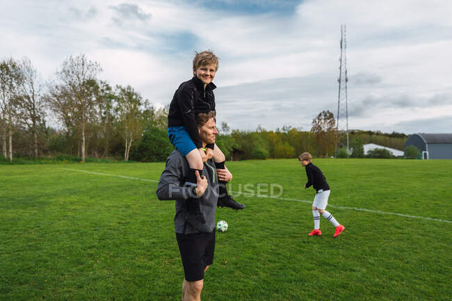 Gai adolescent garçon coups de pied ballon et jouer au football sur le terrain avec père et frère pendant week-end — Photo de stock