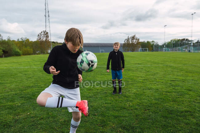 Мальчики-подростки в спортивной форме вместе играют в футбол на зеленом поле летом — стоковое фото