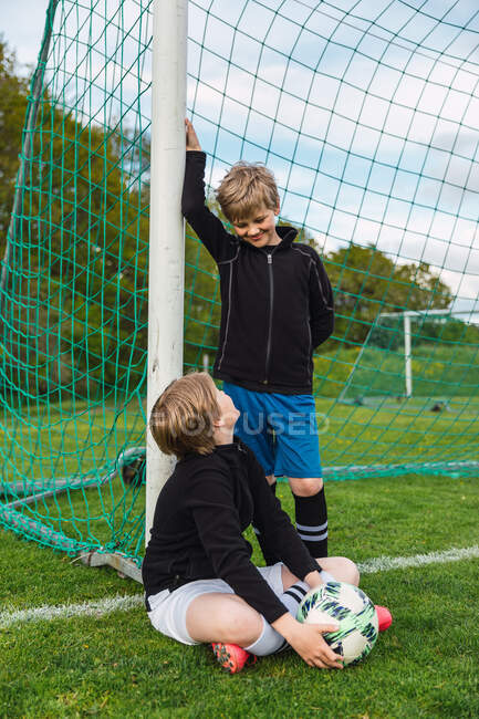 Positive teen football players in sportswear and with ball looking at each other in field — Stock Photo