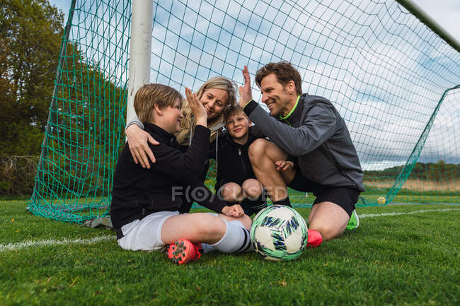 Семья в спортивной одежде дает пять, собираясь на зеленом футбольном поле в выходные — стоковое фото