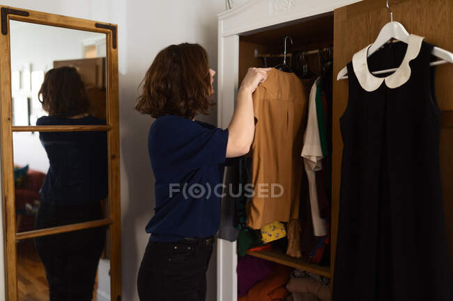 Vista lateral hembra adulta examinando ropa mientras está de pie cerca del armario y seleccionando el atuendo en casa - foto de stock