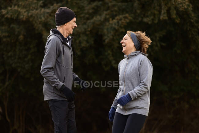 Vista lateral do casal de idosos pulando juntos enquanto ri durante o exercício de fitness ativo na natureza — Fotografia de Stock