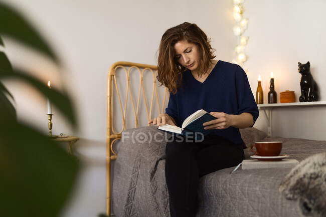 Frau sitzt auf Bett und liest Buch zu Hause — Stockfoto