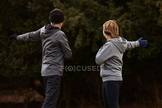 Старая пара в спортивной одежде вытягивает руки во время тренировок в парке и смотрит в сторону — стоковое фото