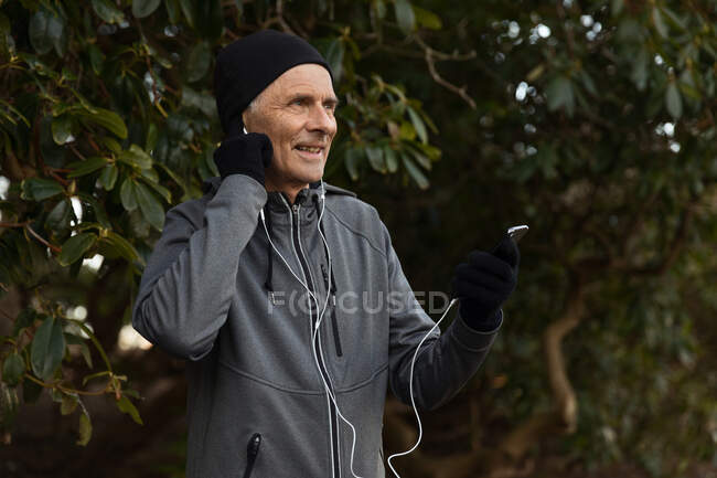 Old male in sportswear listening to music in earphones during outdoor training — Stock Photo
