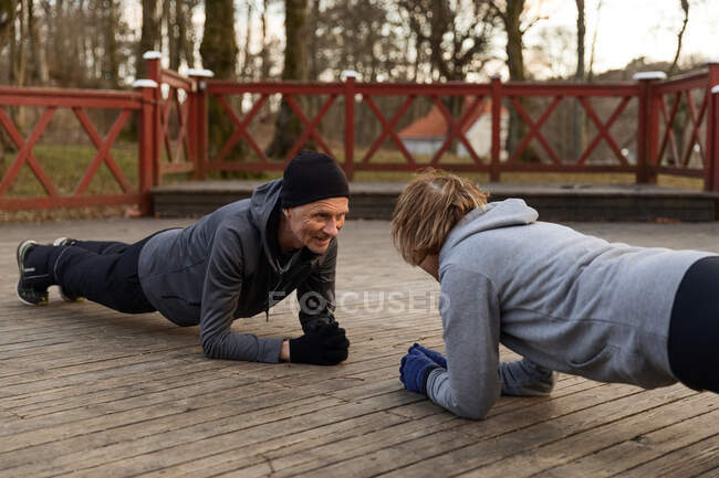Senior couple doing elbow plank exercise on wooden floor during active training in park in autumn day — Stock Photo
