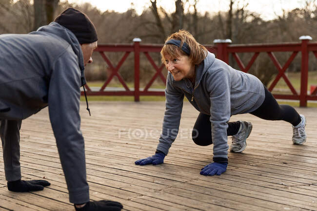 Coppia anziana che fa ginnastica gomito plancia sul pavimento in legno durante l'allenamento attivo nel parco in autunno giorno — Foto stock