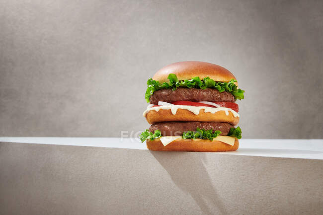 Leckere Doppel-Burger mit Schnitzeln und frischem Salat und köstlichem Käse auf grauem Hintergrund serviert — Stockfoto