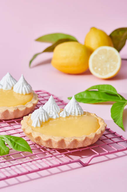High angle of tasty lemon tarts with whipped cream served on pink background with fresh citruses — Stock Photo