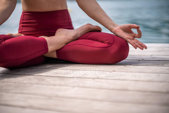 Sereno feminino sentado em Padmasana no cais de madeira e meditando enquanto pratica ioga com gestos mudra perto do lago no verão — Fotografia de Stock