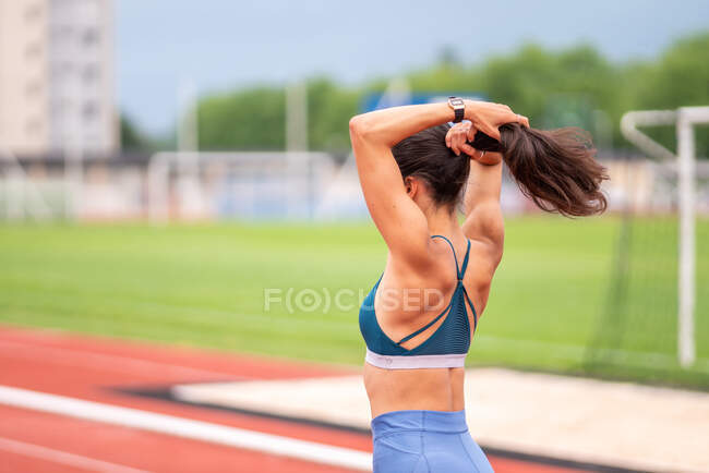 Вид збоку на невпізнавану спортсменку, яка коригує хвіст під час підготовки до бігу на трасі стадіону — стокове фото