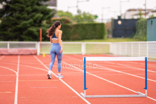 Обратный вид на неузнаваемую спортсменку, идущую на стадионе возле барьера во время легкой атлетики — стоковое фото