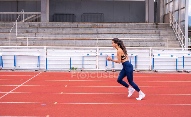 Vista lateral do atleta feminino correndo no estádio durante o treino de pista e campo — Fotografia de Stock