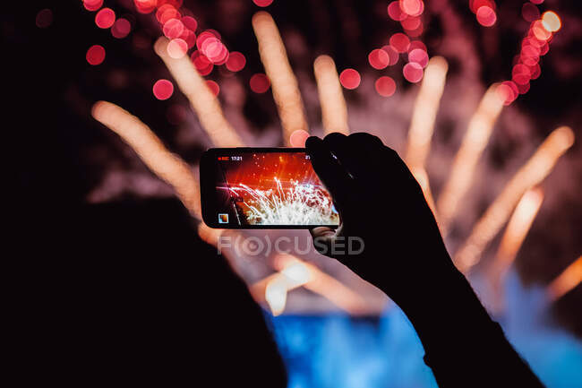 Recadrer visionneuse anonyme enregistrement vidéo de feux d'artifice lumineux sur téléphone portable pendant le spectacle de lumière la nuit sur fond flou — Photo de stock