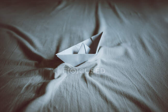 From above of paper boat on creased textile representing lake with waves in daylight — Stock Photo