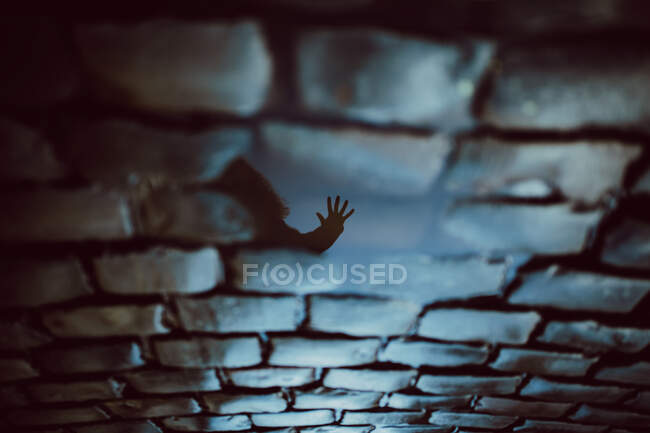 High angle of reflection on wet cobblestone ground of unrecognizable person reaching hand with stop gesture — Stock Photo