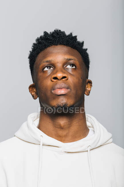 Selbstbewusster ernsthafter junger Afroamerikaner im weißen Kapuzenpullover blickt vor grauem Hintergrund auf — Stockfoto