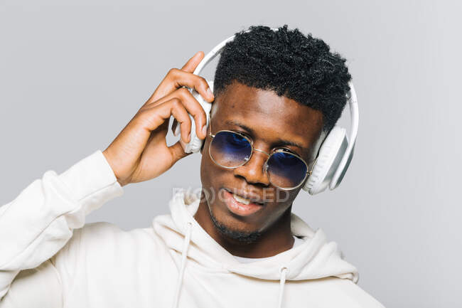 Jovem feliz afro-americano hipster cara com capuz branco e óculos de sol na moda ouvir música através de fones de ouvido sem fio — Fotografia de Stock