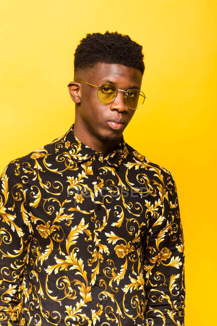 Portrait d'un homme afro-américain sans émotion en tenue tendance debout sur fond jaune en studio regardant la caméra — Photo de stock