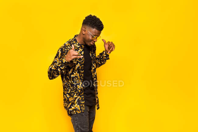 Smiling African American male in trendy outfit showing shaka gesture on yellow background in studio — Stock Photo