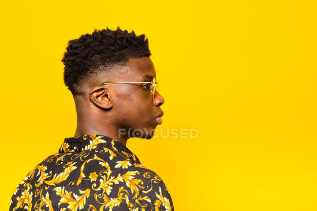 Retrato de hombre afroamericano sin emociones en traje de moda de pie sobre fondo amarillo en el estudio mirando hacia otro lado - foto de stock