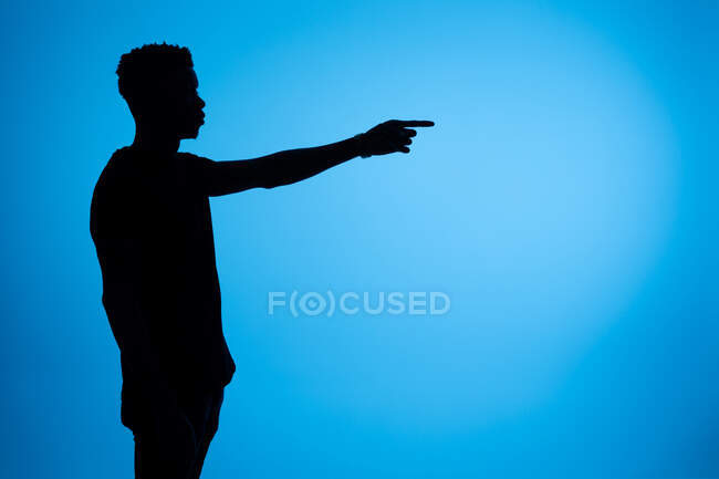 Бічний вид на силует афро-американського чоловіка, що стоїть з витягнутою рукою і вказує на синє тло в студії — стокове фото