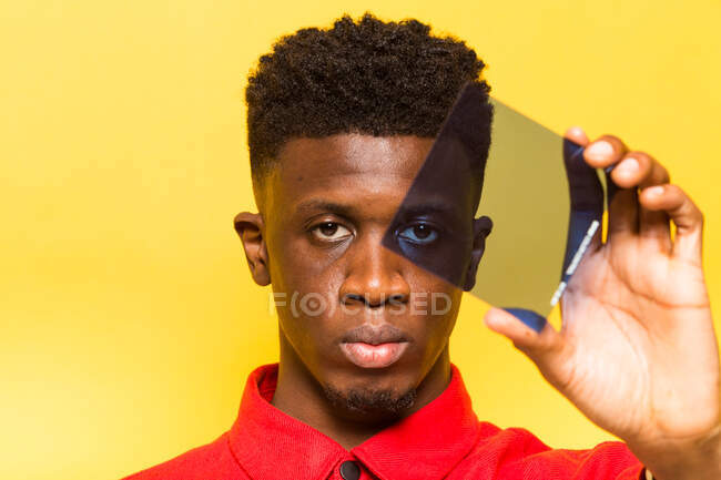 Serious African American male looking at camera through blue color filter on yellow background in studio — Stock Photo