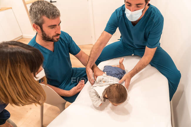 Зверху самець - педіатр обстежує немовлятко на медичному столі в кімнаті з матір 