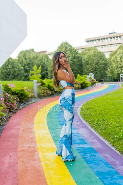 Giovane donna in abito alla moda in piedi sul colorato percorso arcobaleno e guardando la fotocamera — Foto stock
