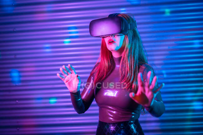 Young woman in VR headset gesticulating and interacting with virtual reality under neon illumination — Stock Photo