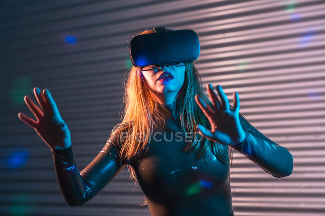 Young woman in VR headset gesticulating and interacting with virtual reality under neon illumination — Stock Photo