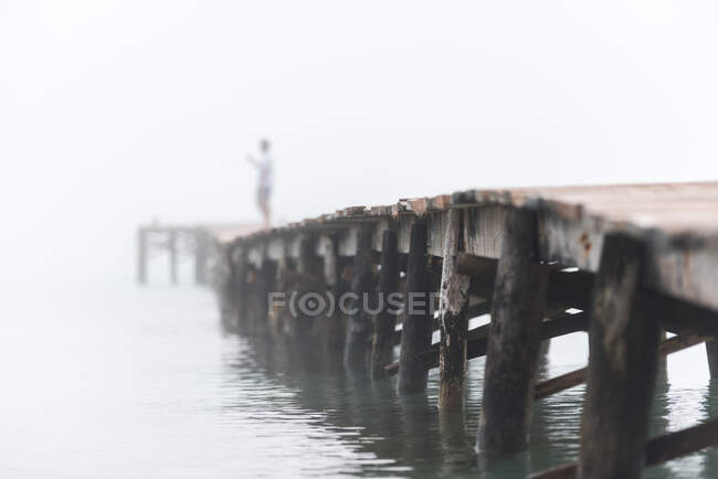 Faceless person standing on wooden pier near sea on Playa de Muro and enjoying misty morning — Stock Photo