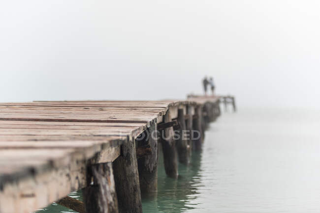 Unkenntliches verschwommenes Pärchen, das am nebligen Morgen an der Playa de Muro auf einem Holzsteg im Meerwasser steht — Stockfoto