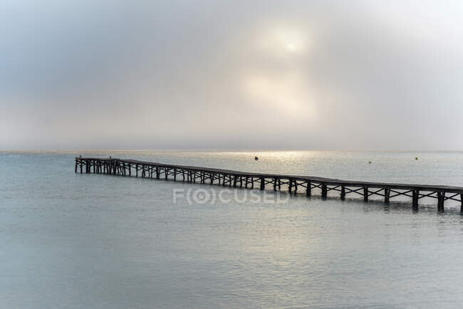 Magnificent scenery of wooden pier located in sea under cloudy sky with sun in morning on Playa de Muro — Stock Photo