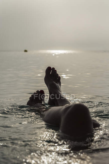 Crop gambe scalze di femmina irriconoscibile sdraiato in acqua di mare e godendo mattina di sole durante le vacanze a Playa de Muro — Foto stock