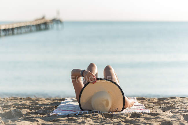 Anonyme femelle en chapeau de paille couché sur le rivage sablonneux le matin et bronzant pendant les vacances d'été sur Playa de Muro — Photo de stock