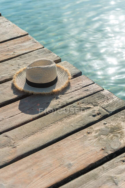High angle of straw sunhat placed on wooden quay near blue sea on sunny day in summer on Playa de Muro — Stock Photo