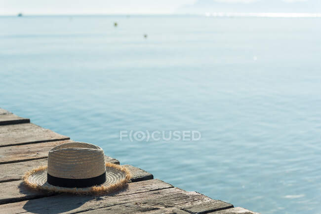 Hohe Winkel Stroh Sonnenhut auf hölzernen Kai in der Nähe des blauen Meeres an einem sonnigen Tag im Sommer an der Playa de Muro platziert — Stockfoto