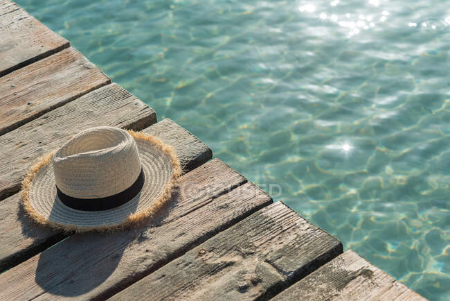 Alto angolo di paglia cappello da sole posto su banchina di legno vicino al mare blu nella giornata di sole in estate su Playa de Muro — Foto stock