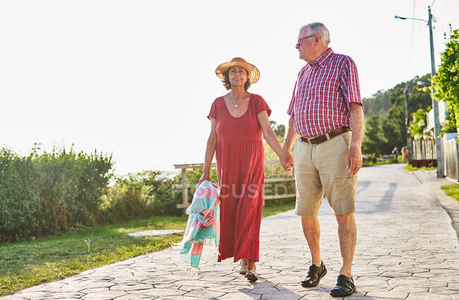 Corps complet de vieux couple aimant se tenant la main tout en se promenant sur le front de mer pavé et profiter de la mer — Photo de stock