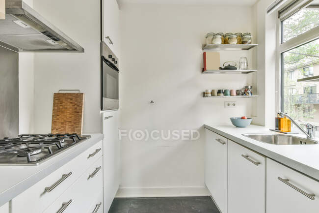 Progettazione creativa di cucina con armadi e stufa contro lavandino e scaffali con vasi in casa durante il giorno — Foto stock