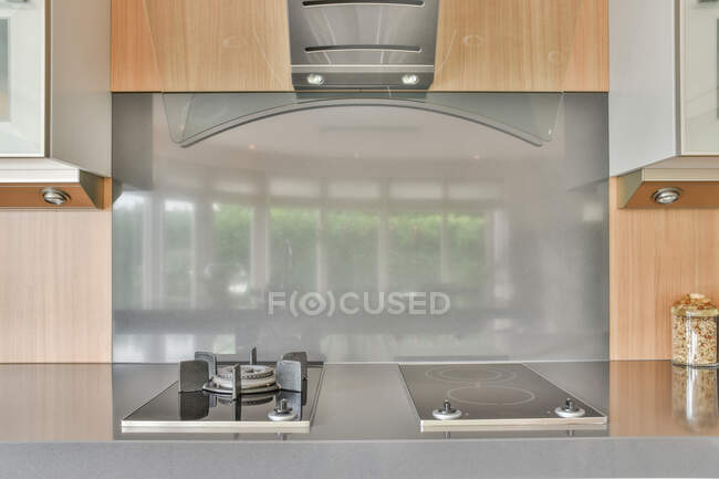 Contemporary kitchen with gas and electric stoves under hood against wall reflecting house in daytime — Stock Photo