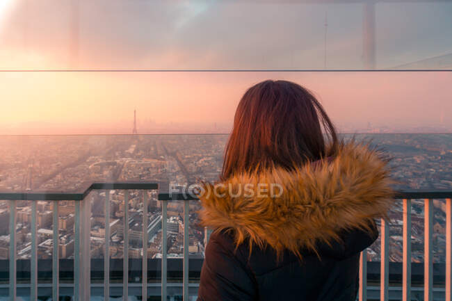 Обратный вид на неузнаваемую женщину-туристку, стоящую на смотровой площадке и любующуюся городским пейзажем с Эйфелевой башней в Париже на закате — стоковое фото
