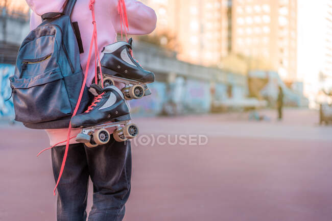 Crop unrecognizable female teenager wearing light pink hoodie and backpack with headphones and roller skates with oink shoelaces — Stock Photo