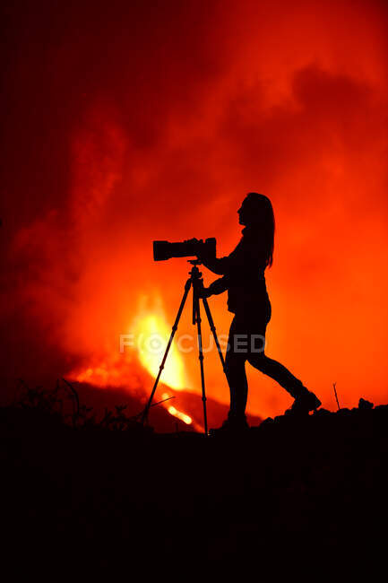 Side view of silhouette of a woman photographing with a telephoto lens and tripod the lava explosion in La Palma Canary Islands 2021 — Stock Photo
