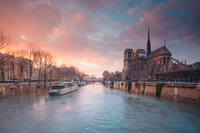 Barco turístico flotando en el agua ondulada del río Sena pasando por la catedral católica medieval de Notre Dame de Paris al atardecer - foto de stock