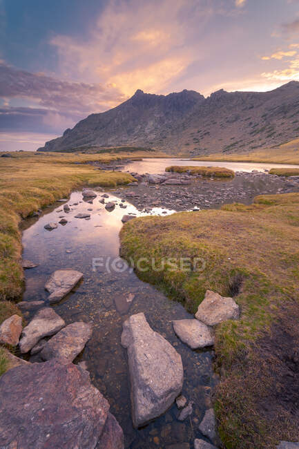 Spectacular scenery of calm lake with rocks against high mountains in Sierra de Guadarrama under colorful cloudy sky at sunrise — Stock Photo