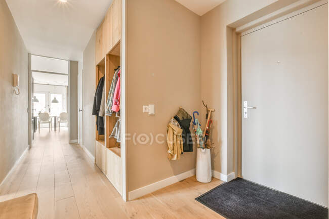 Парасольки, розміщені біля підвісних курток на стіні в коридорі з дерев'яним шафою і світлими стінами в сучасній квартирі — стокове фото