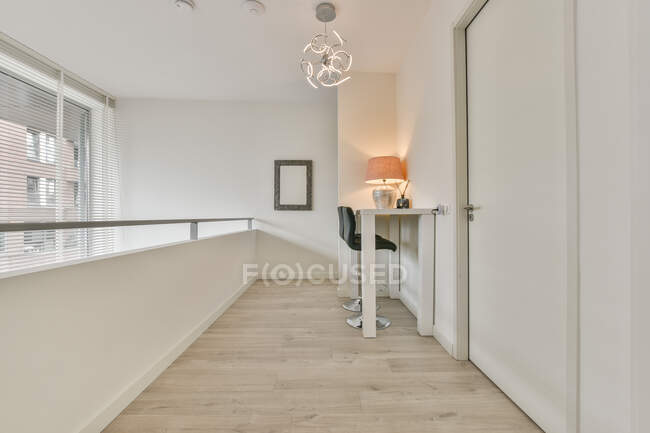 Moderno hall interior con valla contra lámpara en la mesa y sillas en el piso en casa de luz - foto de stock